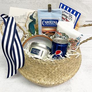 This rattan belly basket is filled with all things Carolina: Carolina Coffee, New Bern skyline kitchen towel, Pepsi, New Bern travel candle, hand crafted bowl from BluSail Golitz Studio in Morehead City, painted oyster from New Bern painter Dianne Ballard, cheese straws, and custom gift tag