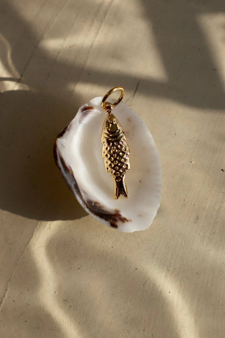 Gold fish pendant on a white shell against a beige background
