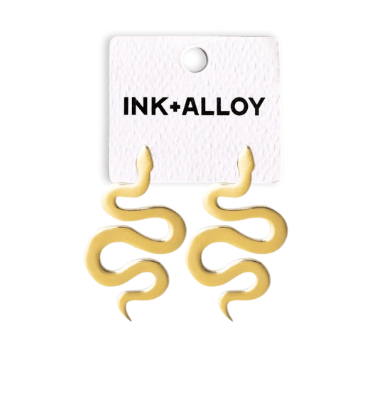 Gold snake-shaped earrings on an Ink+Alloy card against a white background