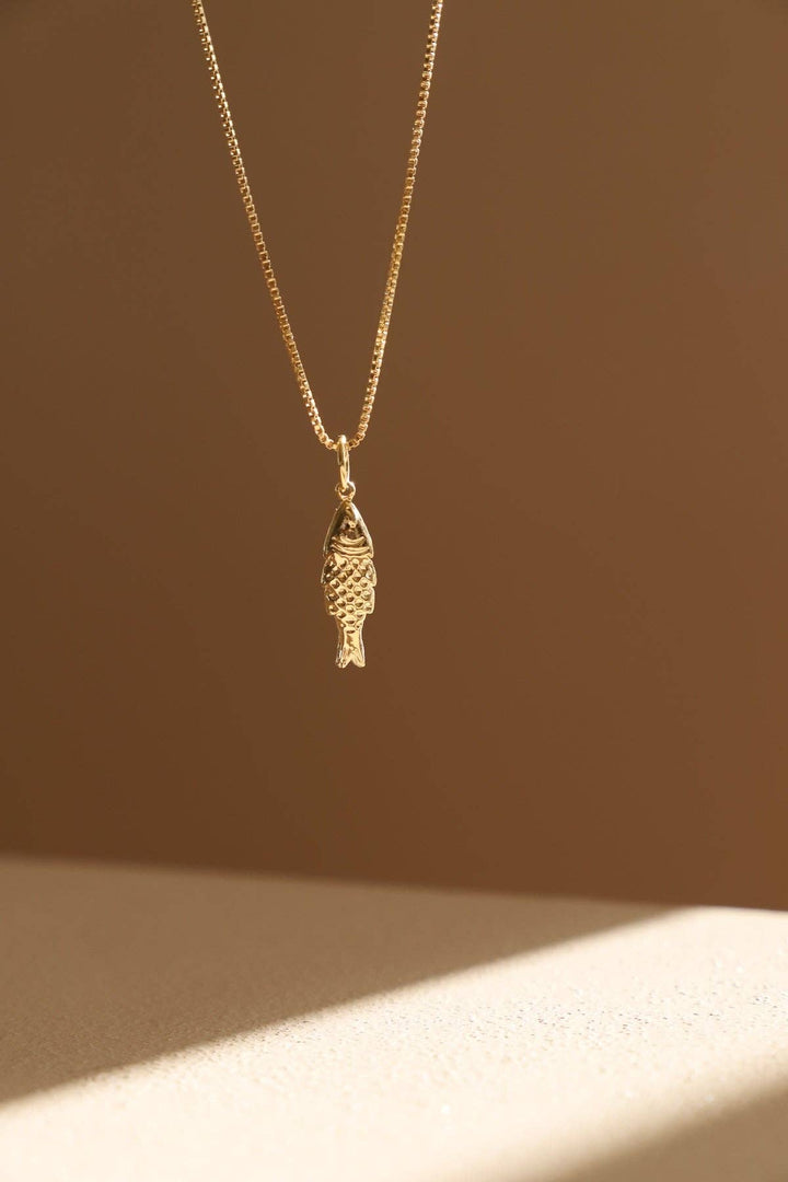 Gold fish-shaped pendant necklace on a beige background