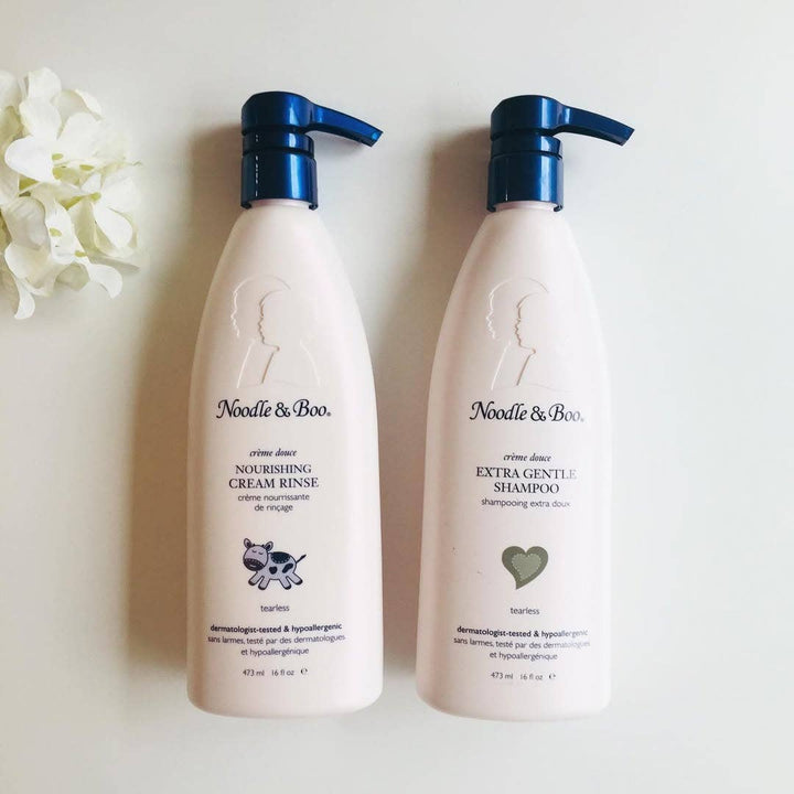 Two bottles of Noodle & Boo shampoo and conditioner on a light background with flowers.