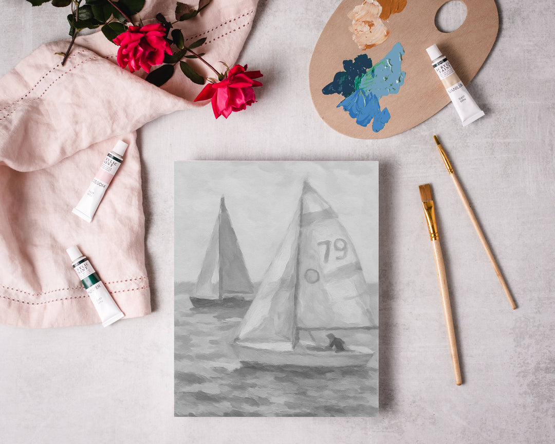 Painting of sailboats on a canvas with art supplies on a light surface