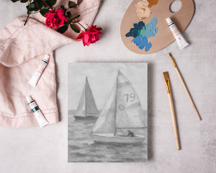 Painting of sailboats on a canvas with art supplies on a light surface