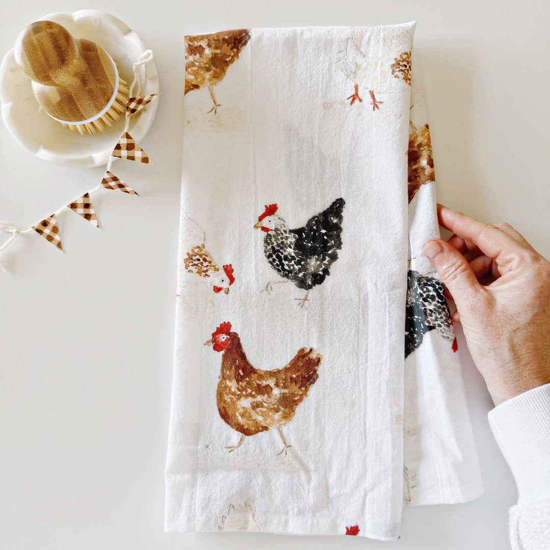 Hand holding a kitchen towel with chicken designs on a light background