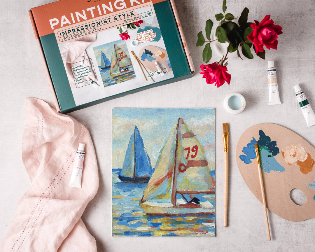 Painting kit with sailboat painting, brushes, and flowers on a table