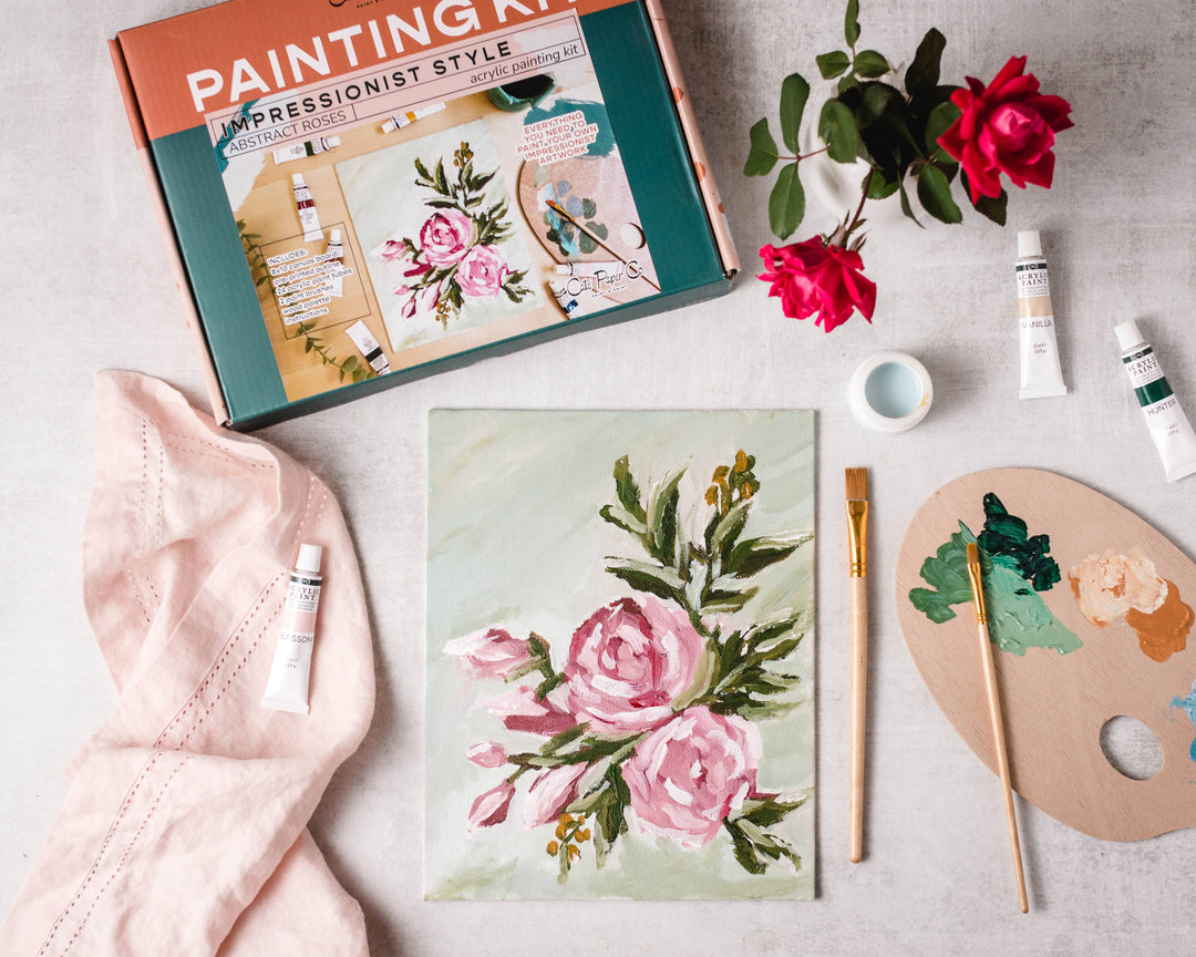 Floral painting kit with completed artwork, paintbrushes, and supplies on a light surface.