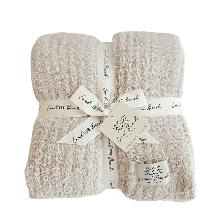 Beige textured blanket with white ribbon and labels on a white background