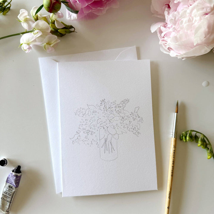 White card with floral design, paintbrush, and flowers on a light surface
