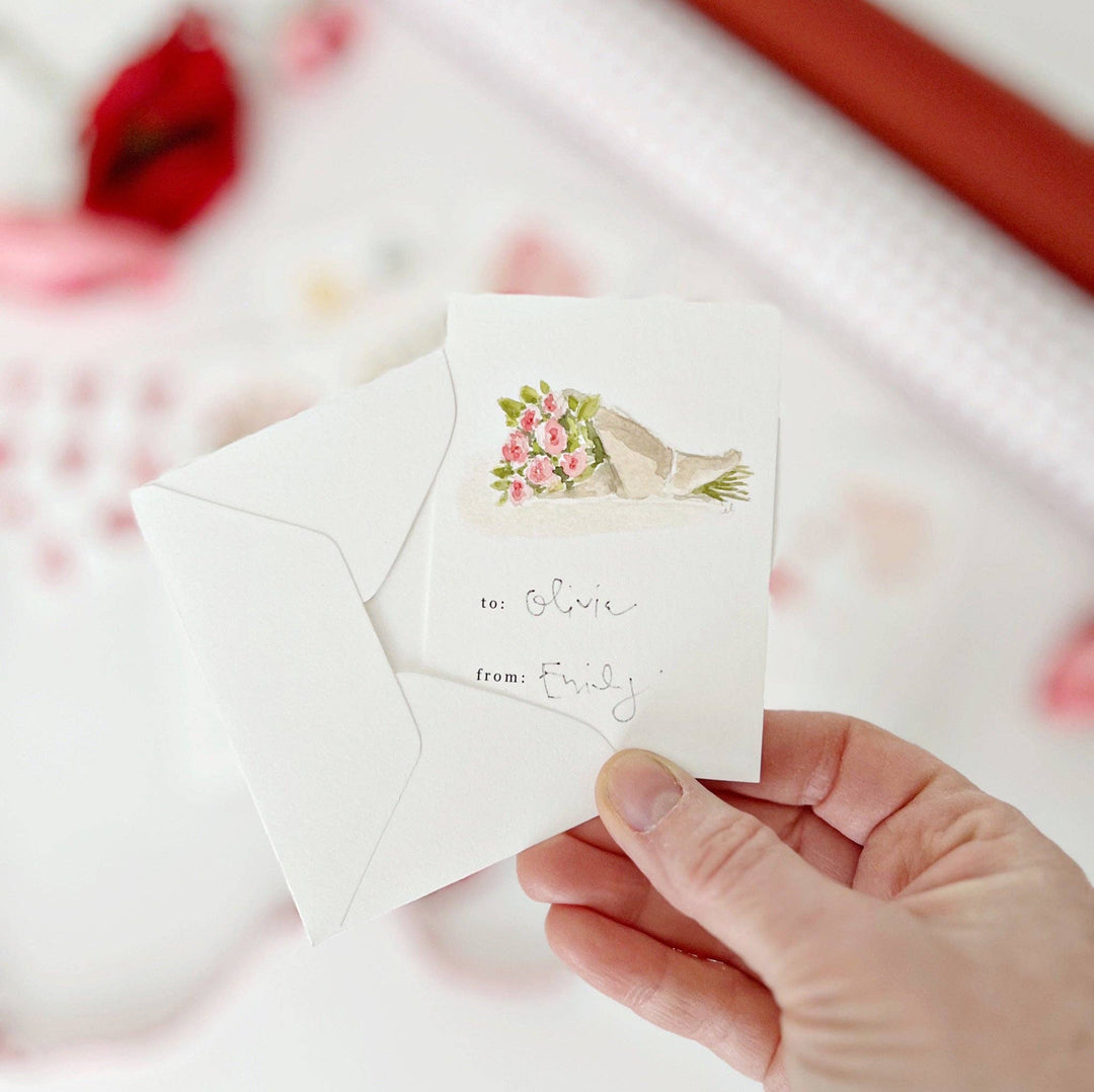 Hand holding a card with a floral design and text, against a blurred background.