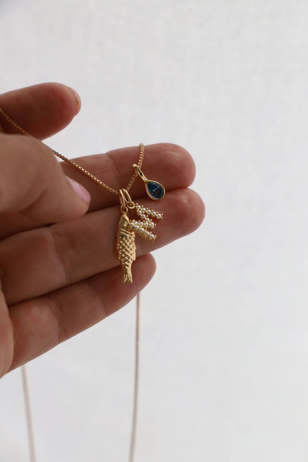 Gold necklace with a leaf pendant held by a hand on a white background