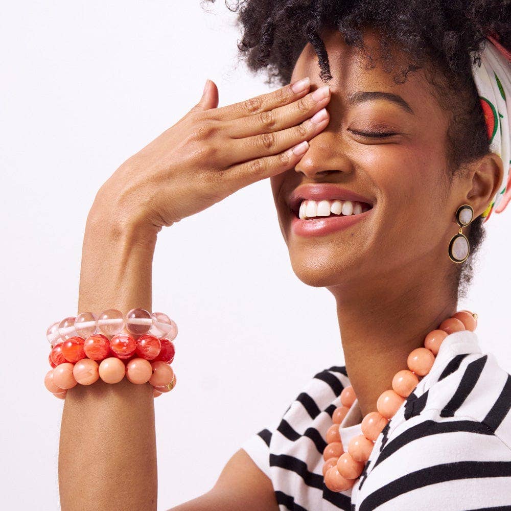 Woman wearing multiple bracelets and a necklace, smiling with one hand covering her eye.