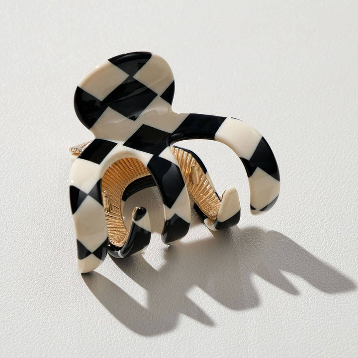 Black and white checkered hair clip with gold accents on a light gray background