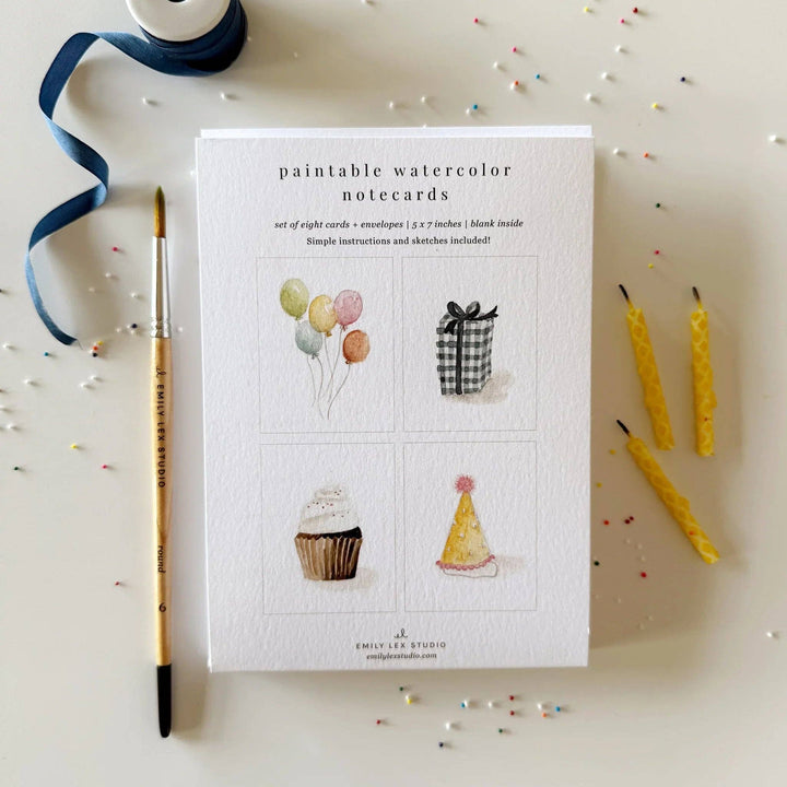Paintable watercolor notecards packaging with a brush, ribbon, and candles on a white background