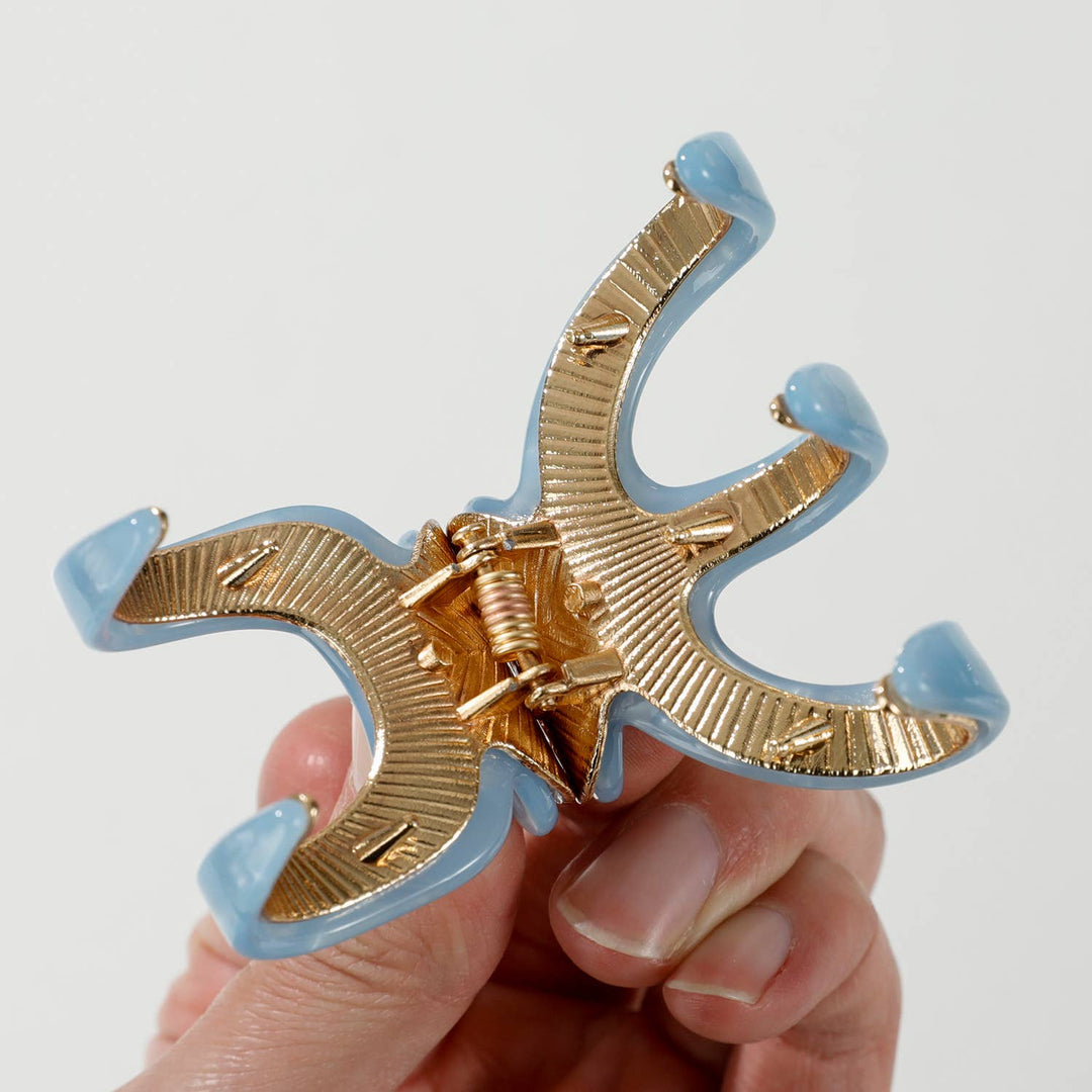 Gold and light blue hair clip held by a hand against a white background