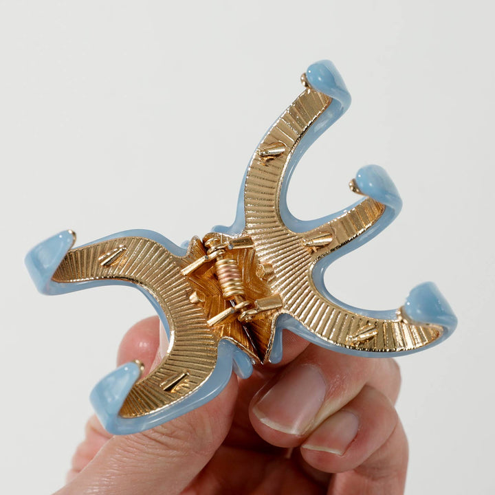 Gold and light blue hair clip held by a hand against a white background