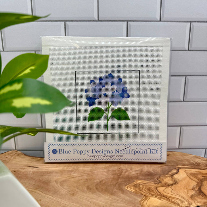 Cross-stitch needlepoint kit with blue flower design on a wooden surface.