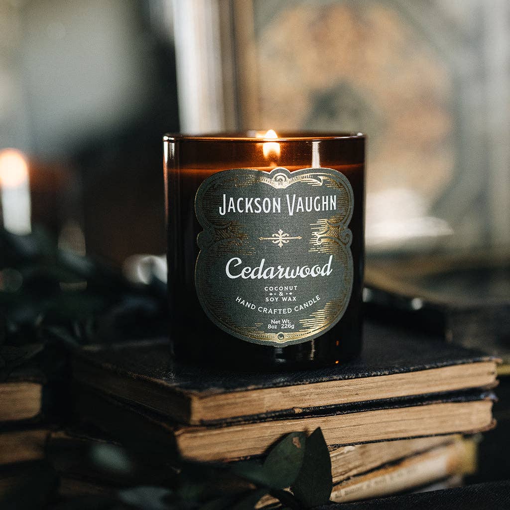 Jackson Vaughn Cedarwood candle on a stack of books with a blurred background