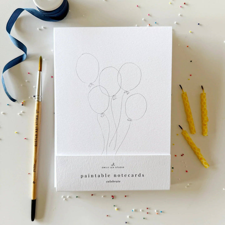 Paintable notecards with balloon design on a white surface with a paintbrush and candles.