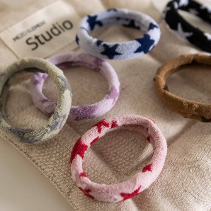 Set of colorful fabric hair ties on a textured surface with 'Studio' branding.