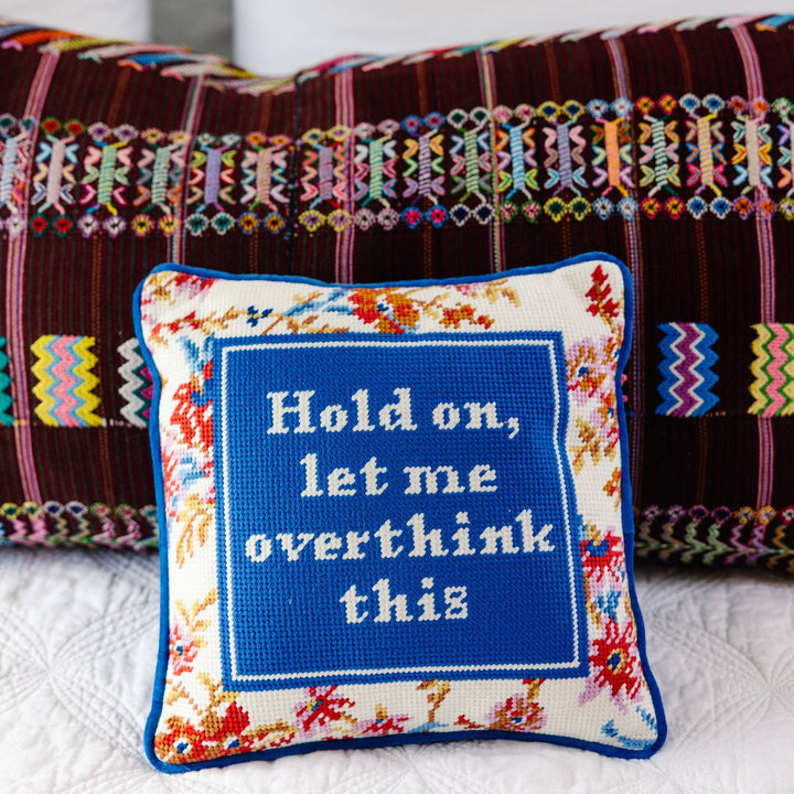 Decorative pillow with embroidered text 'Hold on, let me overthink this' on a colorful background.