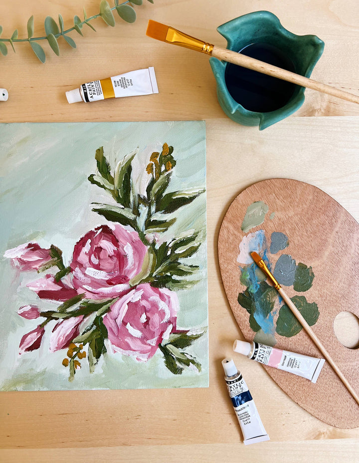 Floral painting on a wooden surface with art supplies including paint tubes, a brush, and a palette.