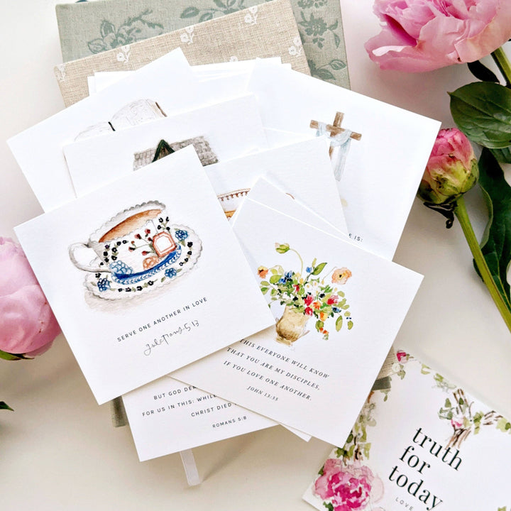 Stack of greeting cards with floral and teacup designs on a light surface with flowers.
