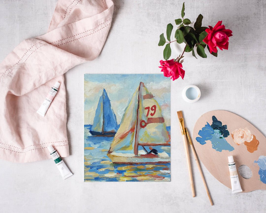 Painting of sailboats on a white surface with art supplies and flowers.