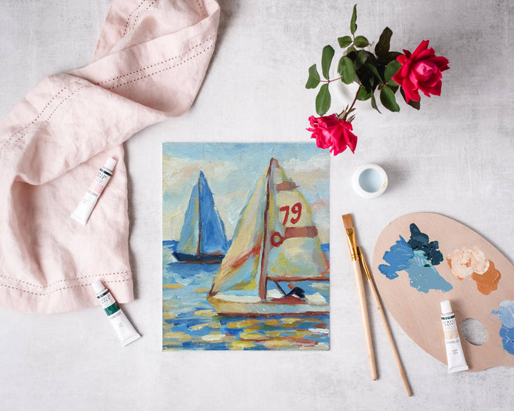 Painting of sailboats on a white surface with art supplies and flowers.