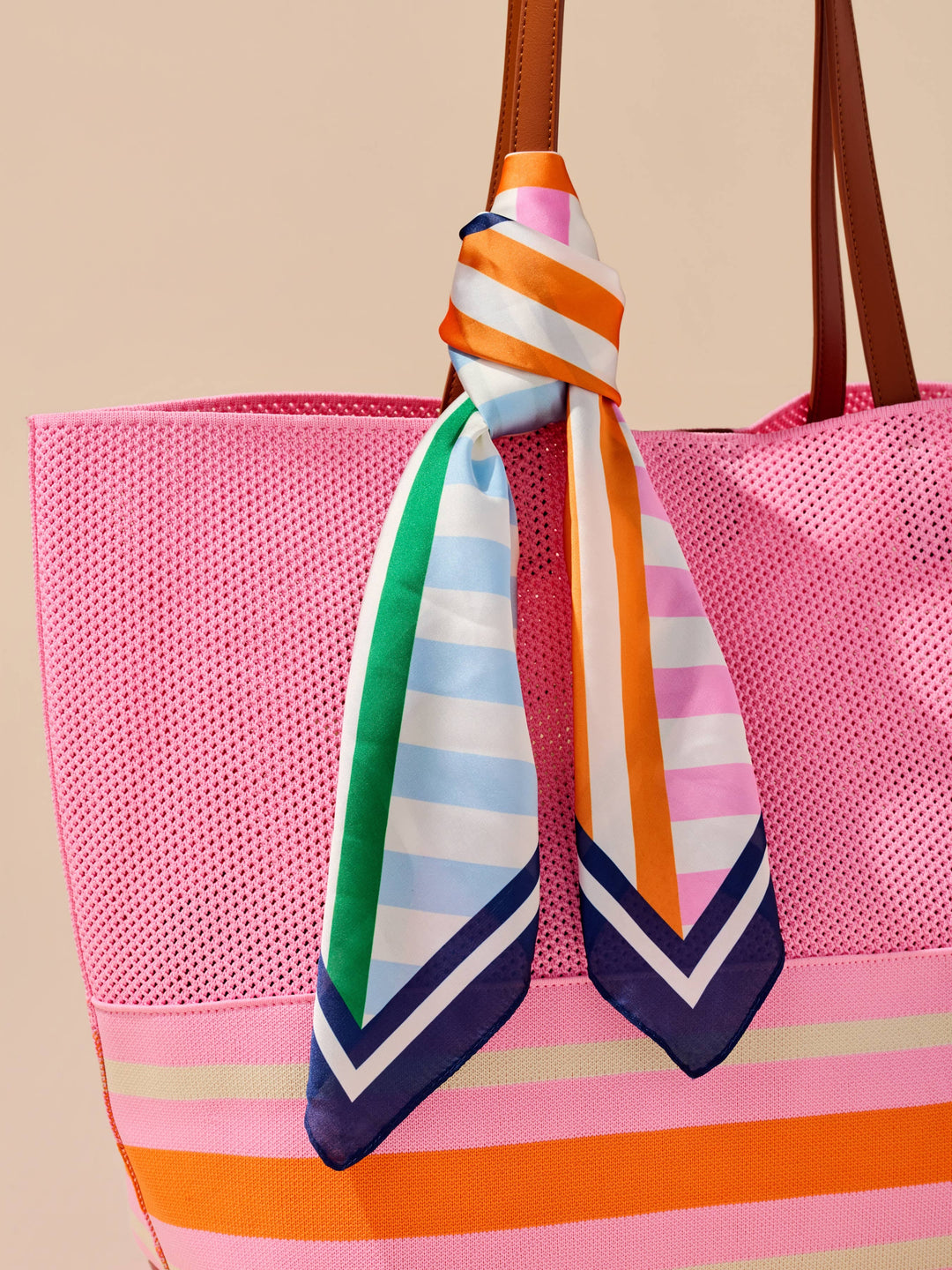 Pink bag with a colorful striped scarf draped over it against a beige background