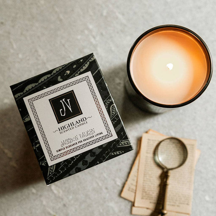Candle and packaging on a textured surface with a magnifying glass and paper.