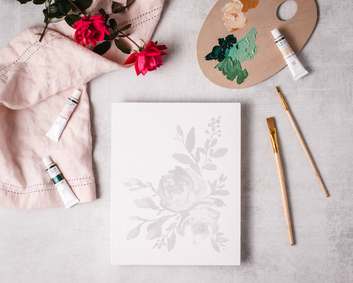 Floral design on paper with art supplies including paint, brushes, and flowers.