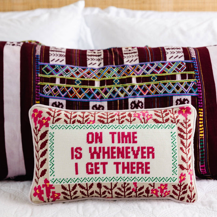 Decorative pillow with embroidered text on a bed with patterned pillows in the background.