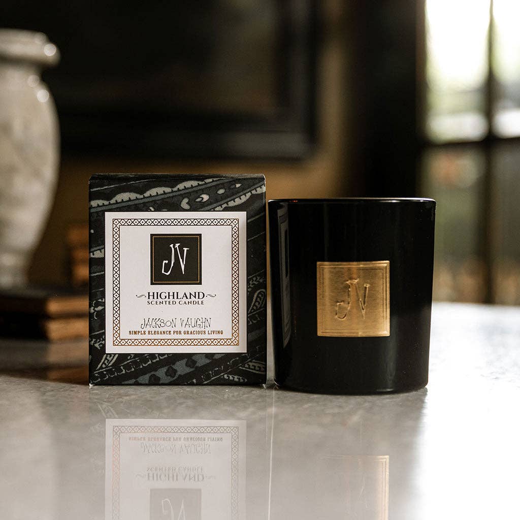 Black candle with gold accent and decorative box on a reflective surface