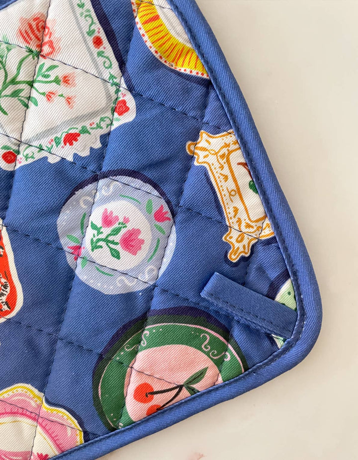 Colorful quilted potholder with floral and abstract designs on a beige background