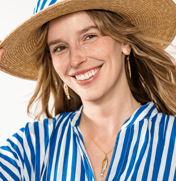 Woman wearing a straw hat and blue and white striped shirt on a white background
