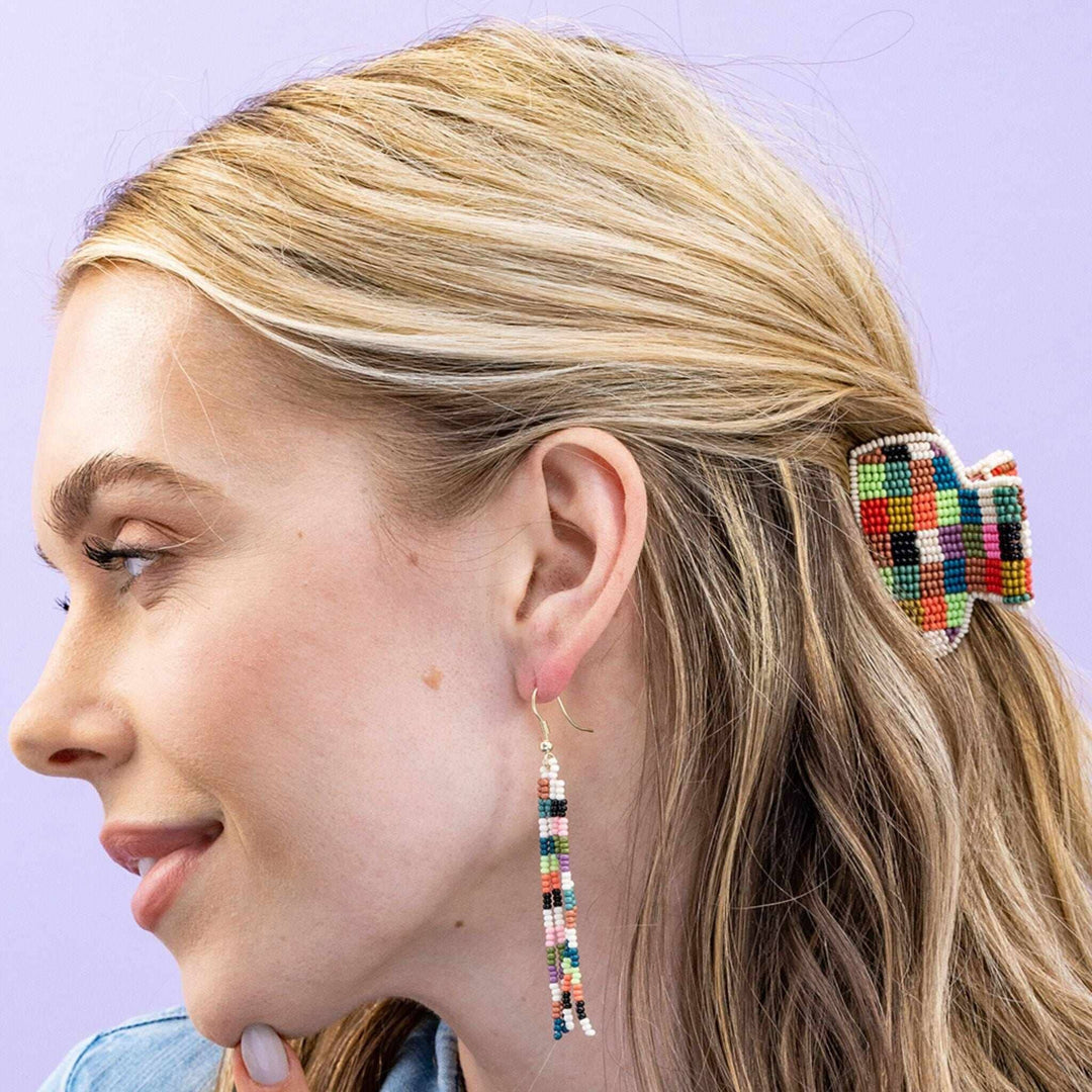 Close-up of a person wearing colorful beaded hair accessory and earrings against a light purple background