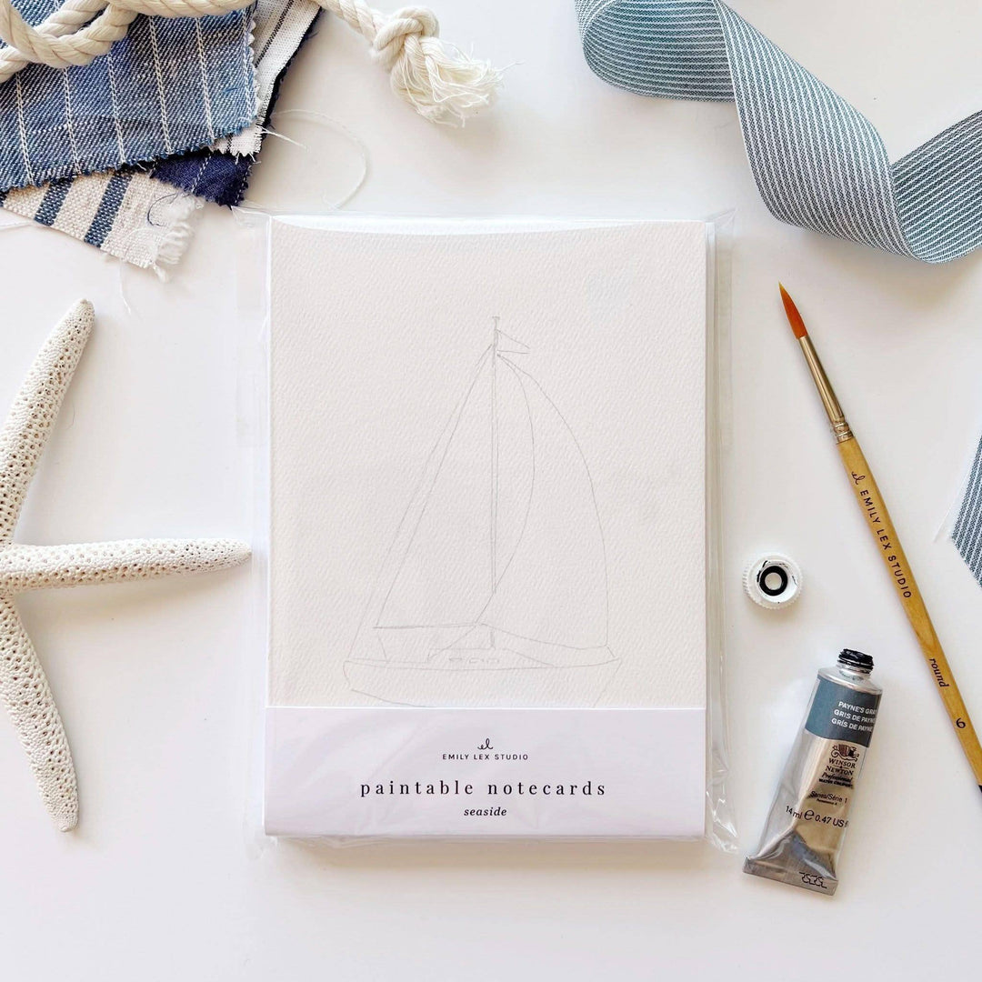 Paintable notecards with sailboat design on a white surface with art supplies.