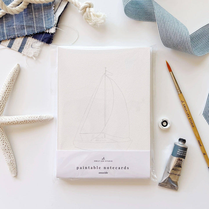Paintable notecards with sailboat design on a white surface with art supplies.