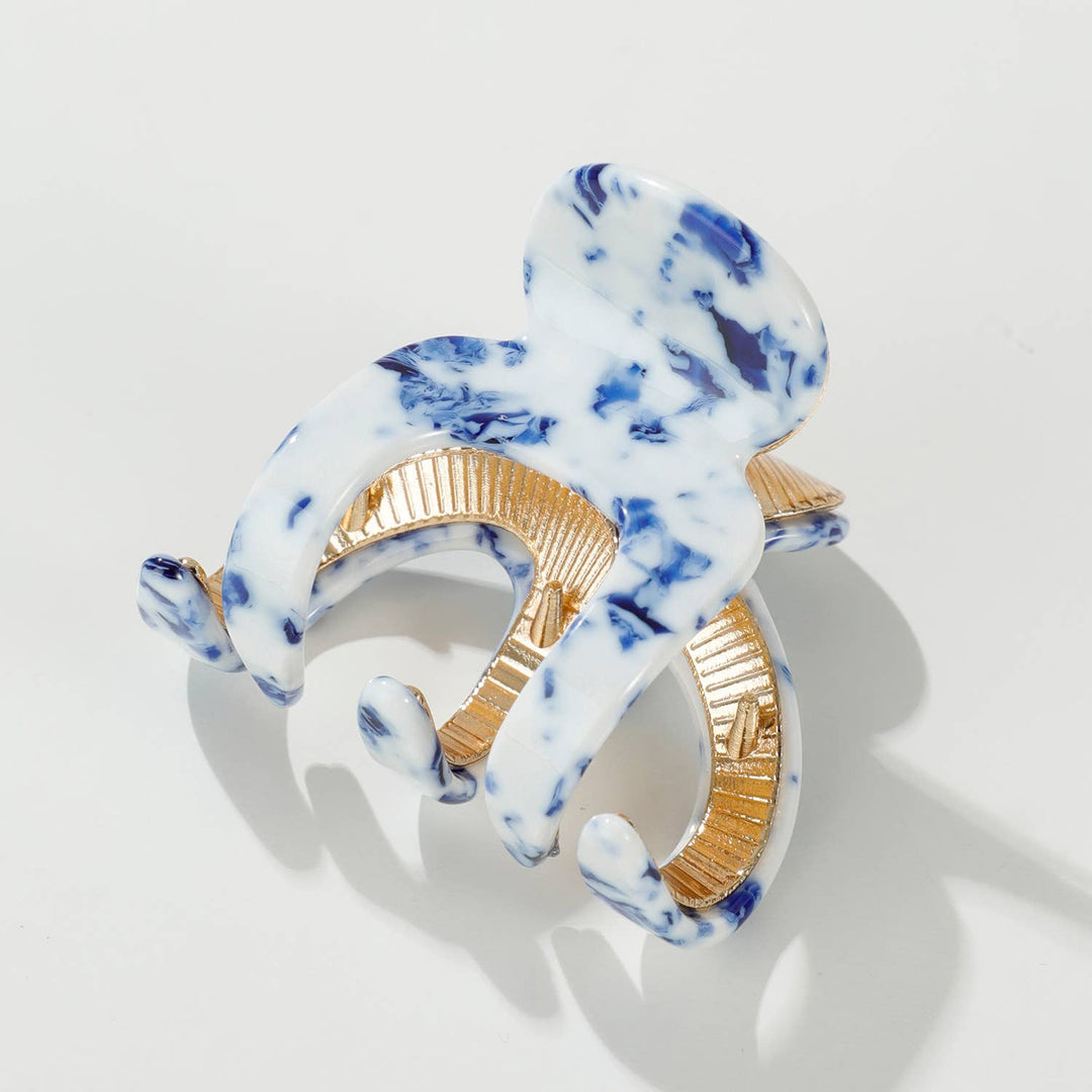 Marble-patterned hair clip with gold accents on a light gray background