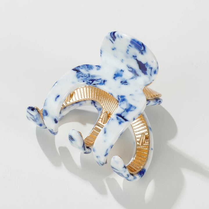 Marble-patterned hair clip with gold accents on a light gray background