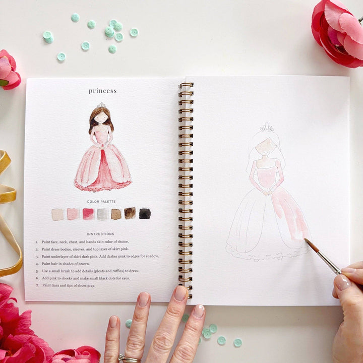 Open book with illustrations of a princess and color palette, surrounded by decorative elements.