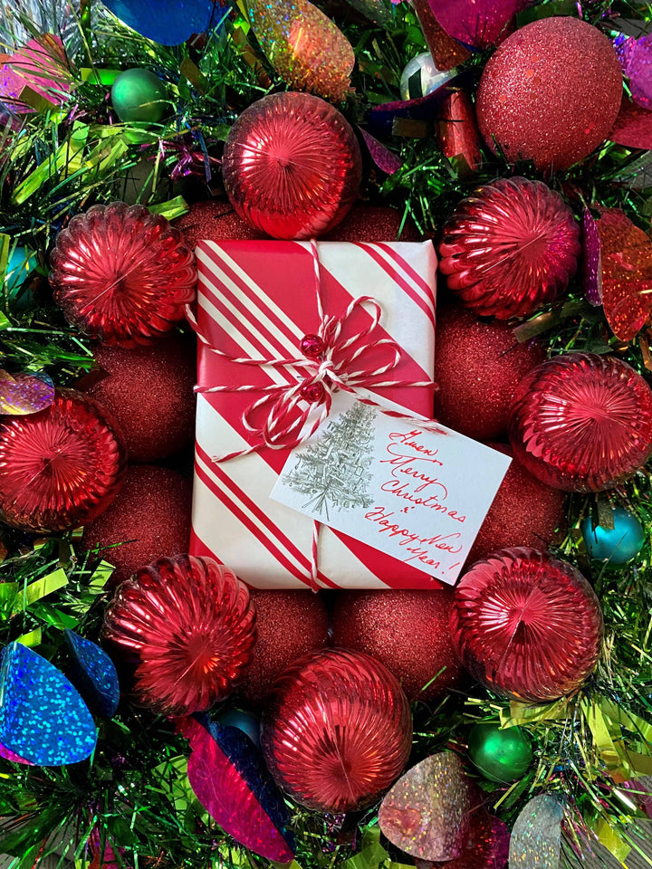 Gift box with a card surrounded by red ornaments and green tinsel with christmas tree gift tag