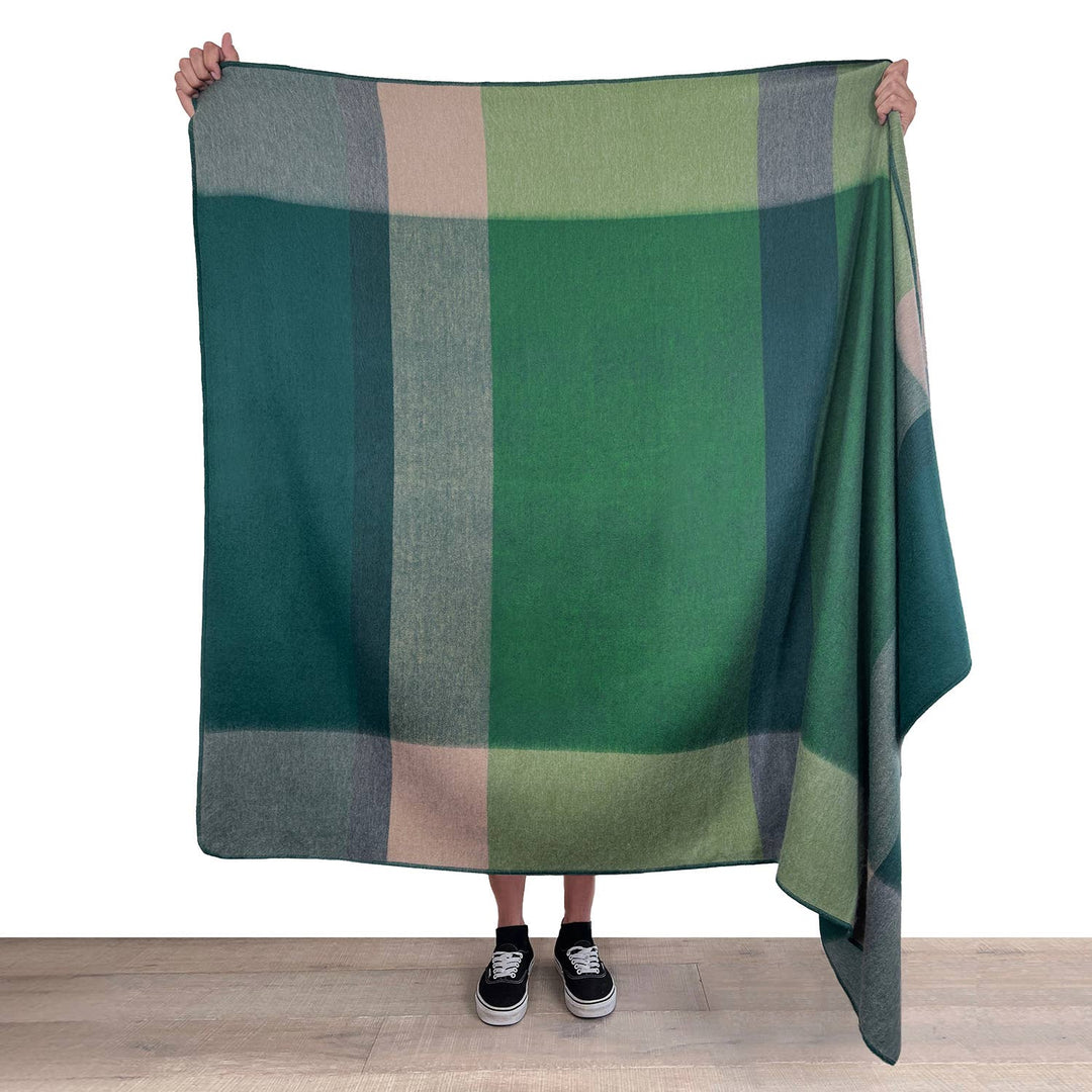Person holding a green plaid blanket on a white background