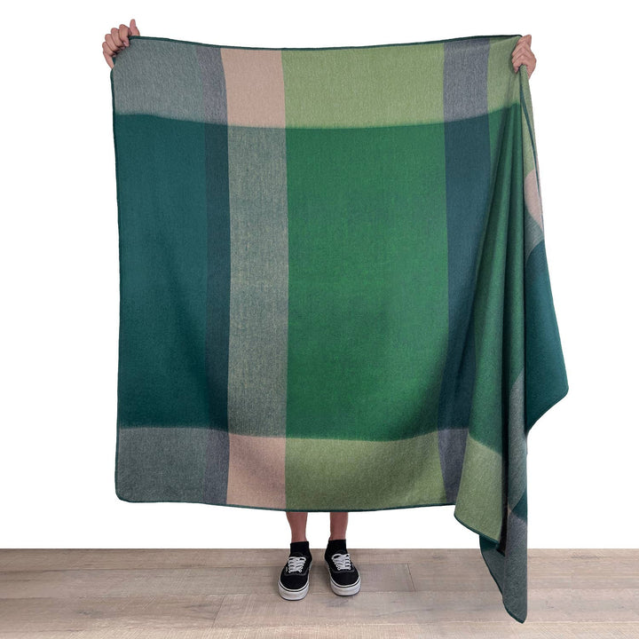 Person holding a green plaid blanket on a white background