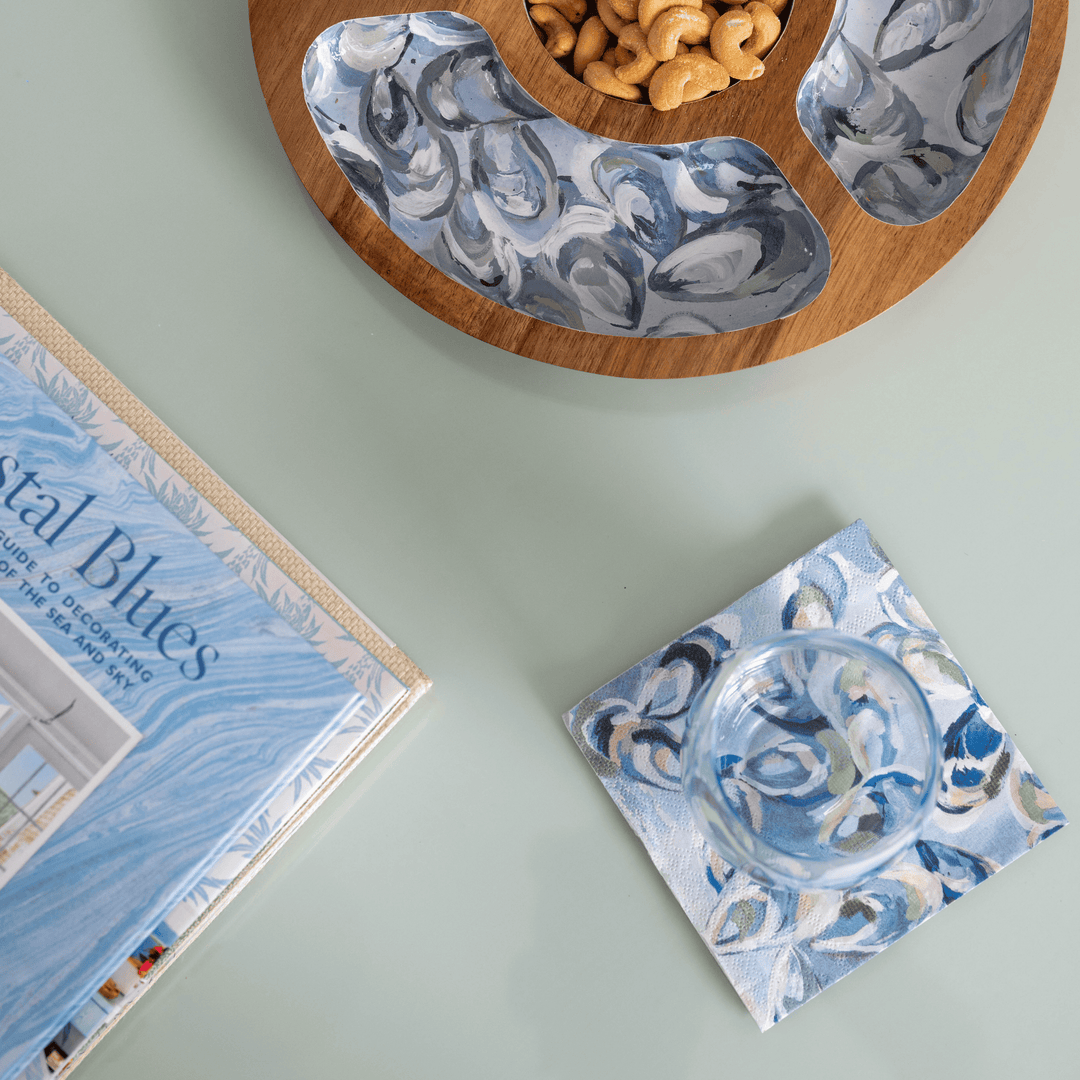 Oyster print cocktail napkins with on a light green surface, next to a book titled 'Nautical Blues'.