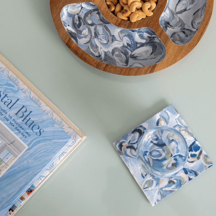 Oyster print cocktail napkins with on a light green surface, next to a book titled 'Nautical Blues'.