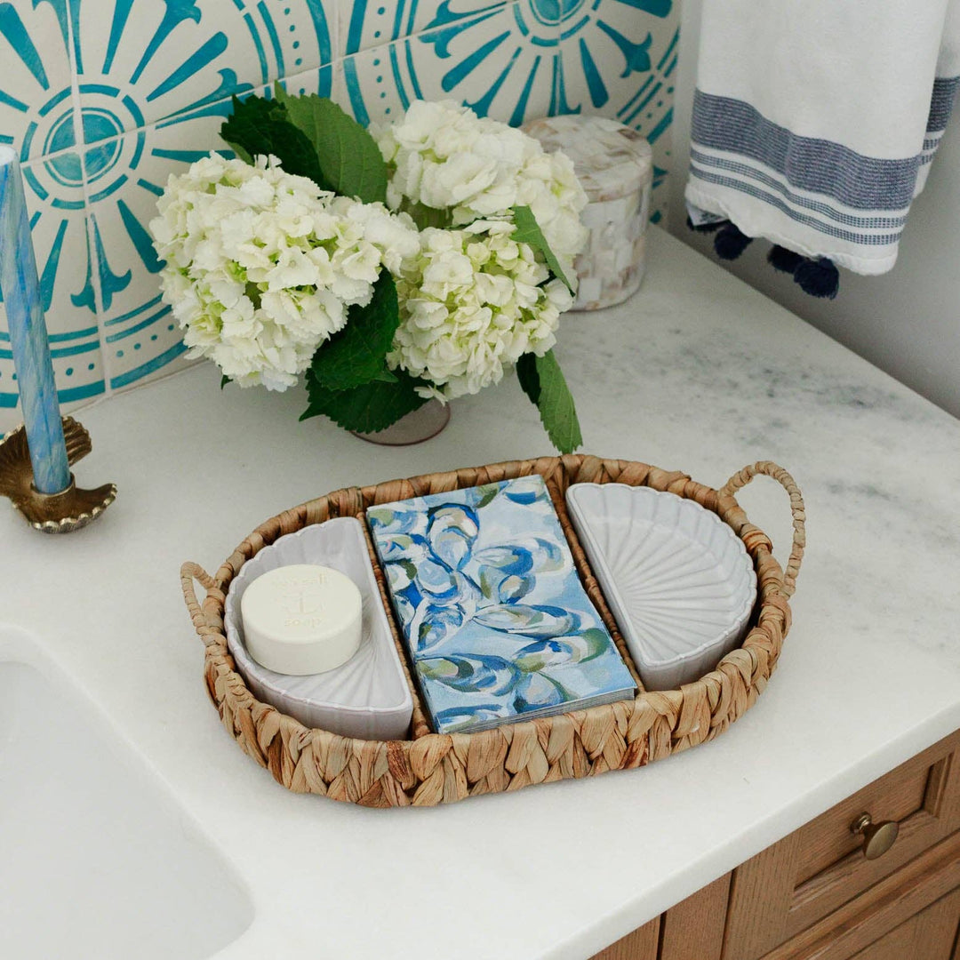 Decorative tray with atlantic reef guest towels, soaps and a candle on a bathroom counter, featuring a floral arrangement and decorative tiles.