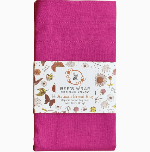 A folded bright pink fabric bread bag wrap with a white paper label wrapped around the middle. The label features floral illustrations and reads 'BEE'S WRAP Artisan Bread Bag'.