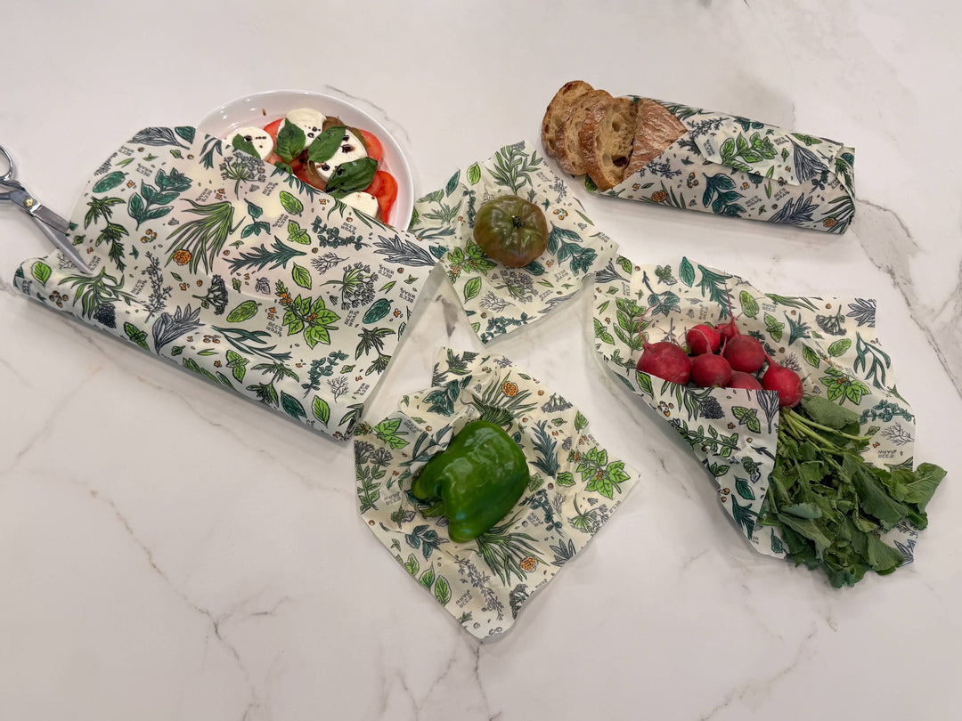Set of floral-patterned beeswax wraps on a marble surface with fruits and vegetables.