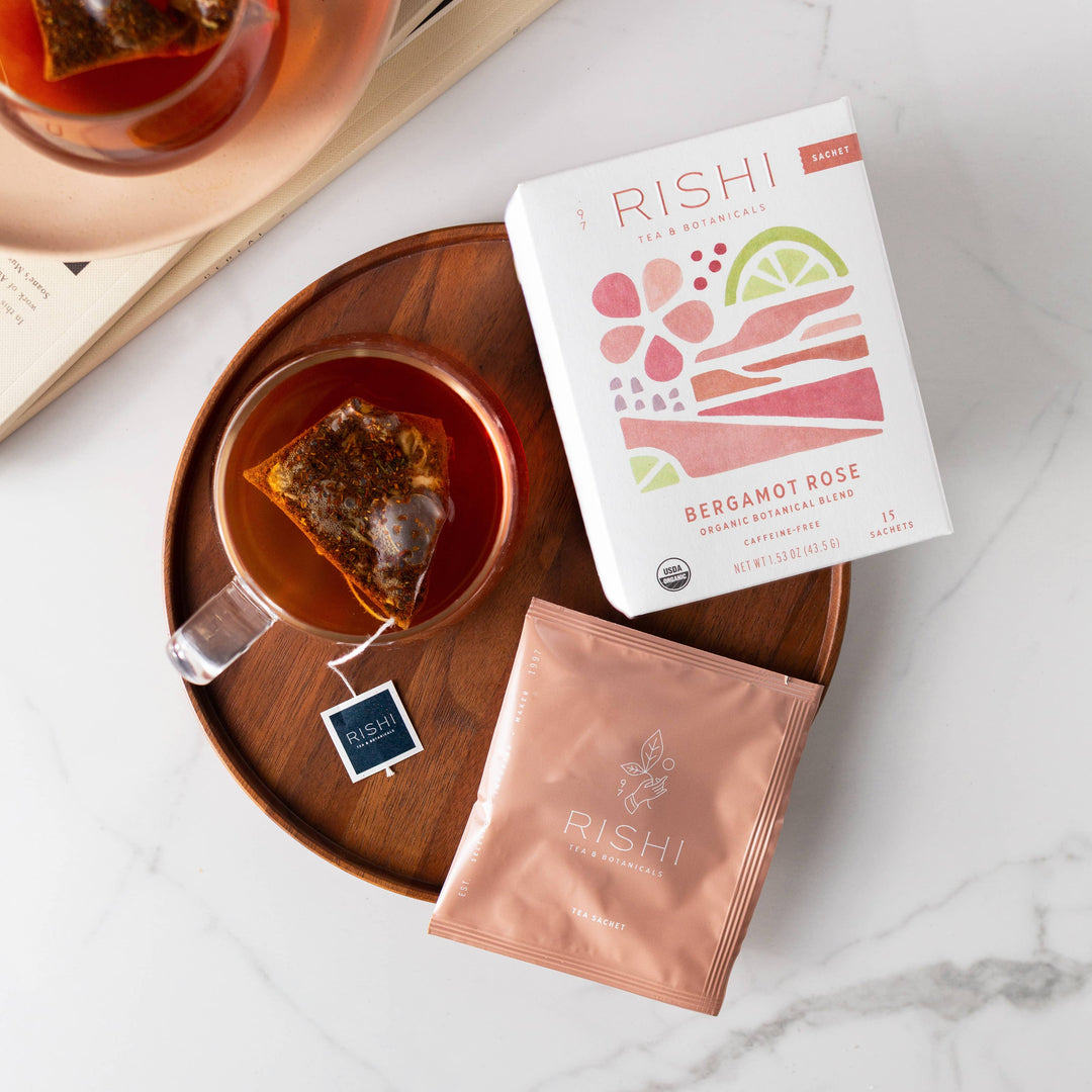 Rishi tea bags and packaging on a marble surface with a wooden tray.